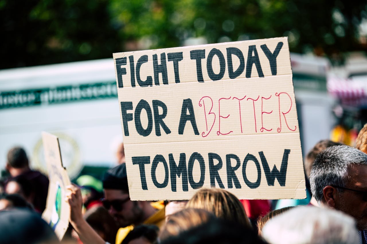Crowd holding a protest sign with Fight Today for a Better Tomorrow, outdoors and during the day.