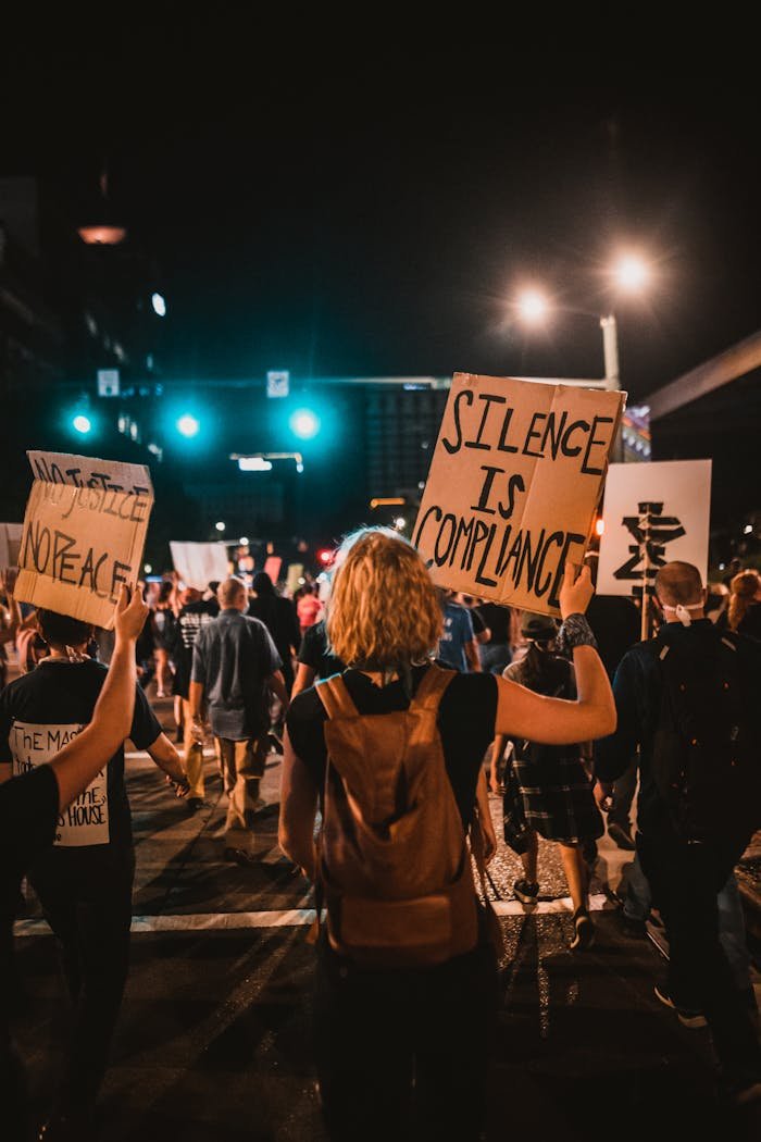 Activists gather at night for a protest in the city, holding signs and expressing their message.